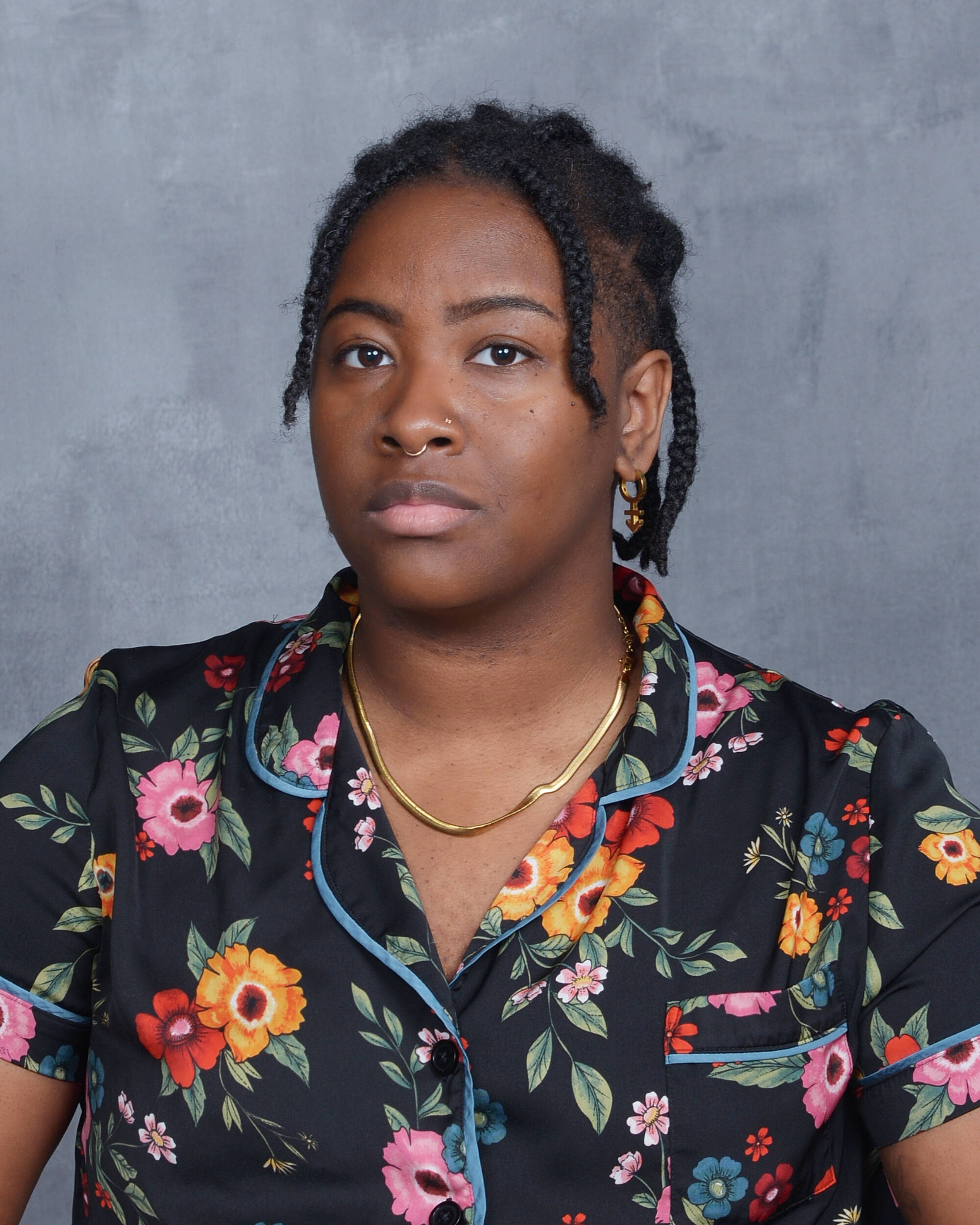 D with a black, floral button down and gold chain. They have just shy of shoulder length braids and an undercut.